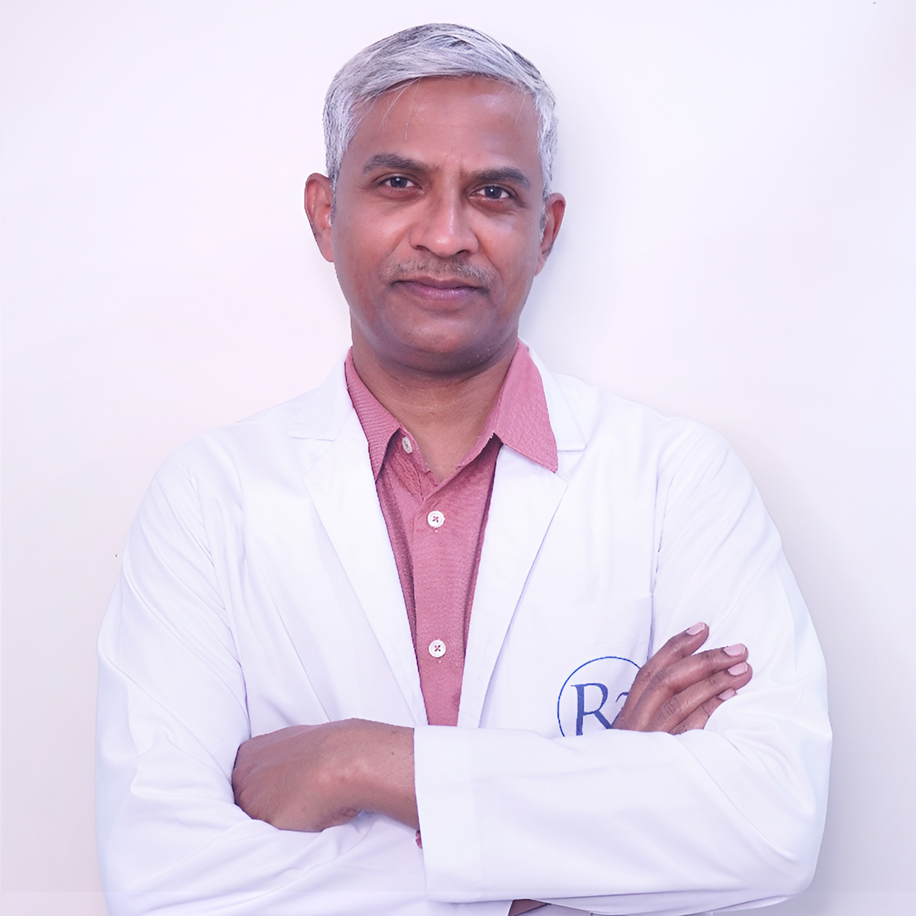 Portrait of Dr. Deepak Bachu, a male urologist wearing a white coat and stethoscope, smiling, vertical rectangle photo