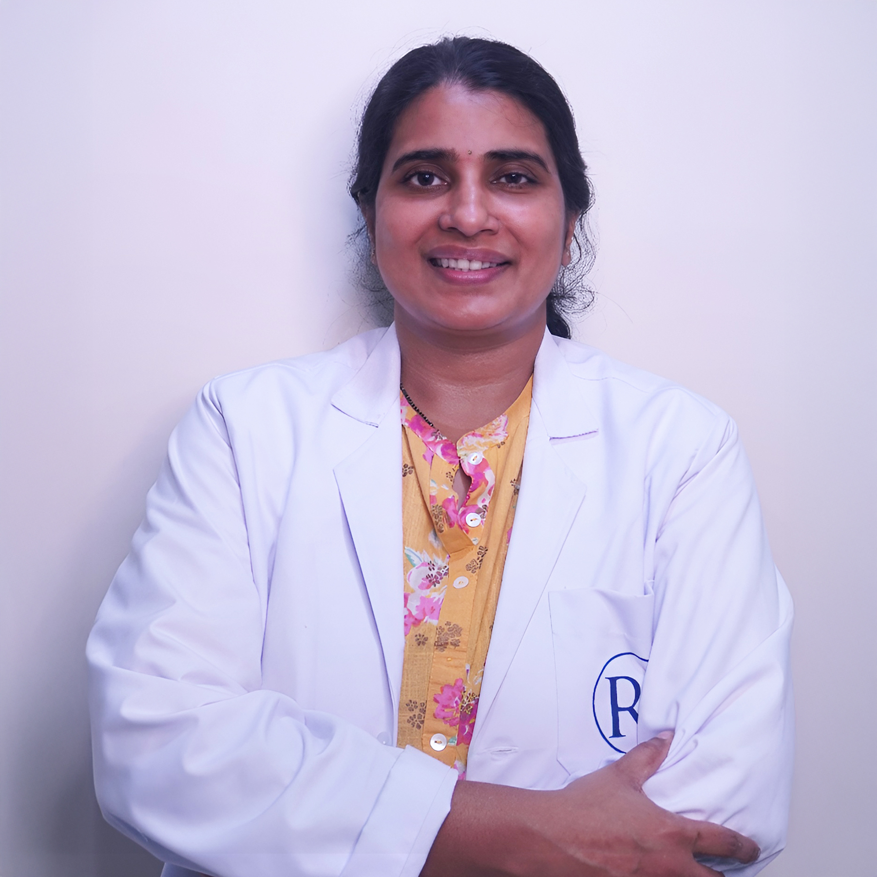 Portrait of Dr. Prathima K, a female dermatologist, smiling and wearing a white coat, vertical rectangle photo