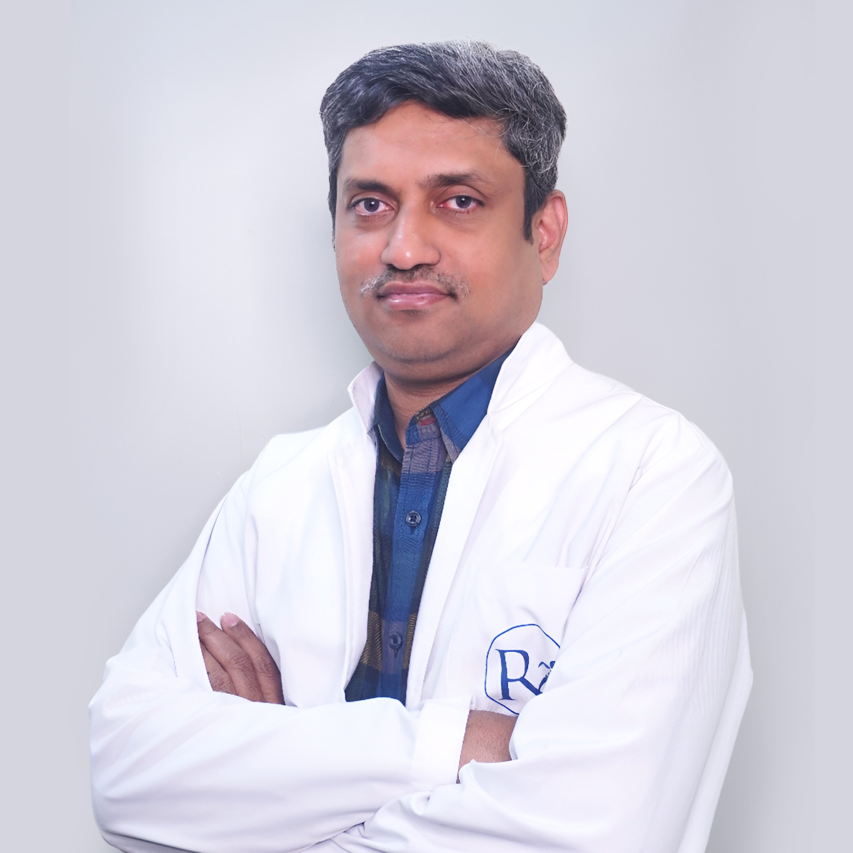 Portrait of Dr. V. Sharath Chandra, a male orthopaedician, smiling and wearing a white coat, vertical rectangle photo